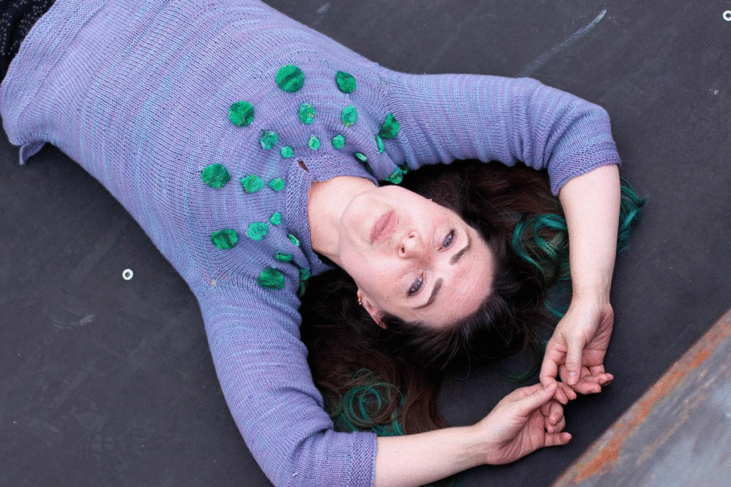 Woman on her back wearing the Circle Dance Sweater and blowing gum bubble