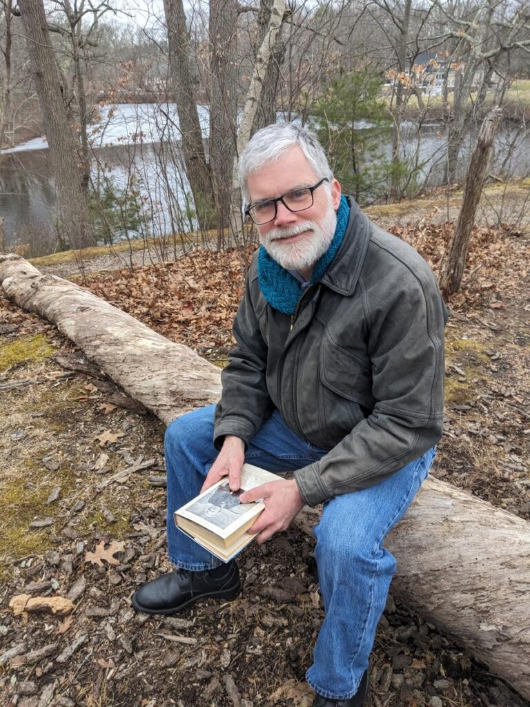 Man wearing Herringbone Hexagonal Scarf while reading a book and sitting on a log